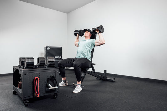 An athlete does a seated shoulder press with adjustable dumbbells.